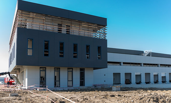 Dettaglio di facciata di nuovo capannone industriale e palazzina uffici in fase di costruzione, con struttura moderna grigia e blu scuro. Servizio fotografico per imprese di costruzione e developer immobiliari.