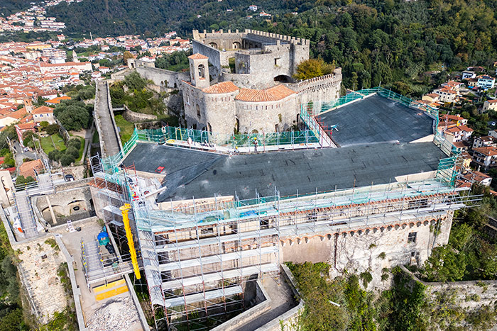 Foto aerea di cantiere per il restauro di un castello storico in Italia. Si vedono i ponteggi montati attorno alle mura e il tetto coperto da guaine impermeabili, a documentazione della riqualificazione storica in corso.