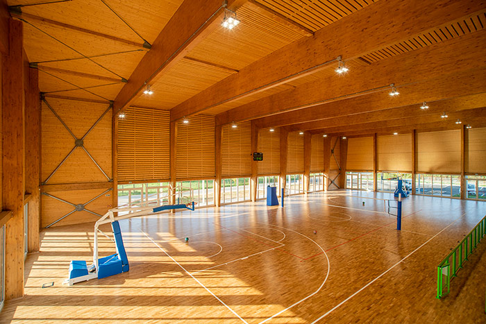 Interno di palazzetto dello sport o palestra con pavimento in legno e grande struttura del tetto in legno lamellare.